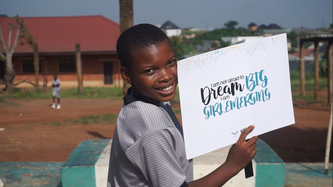 A girl holding a Girls Emerging card that reads “I am not afraid to dream big”