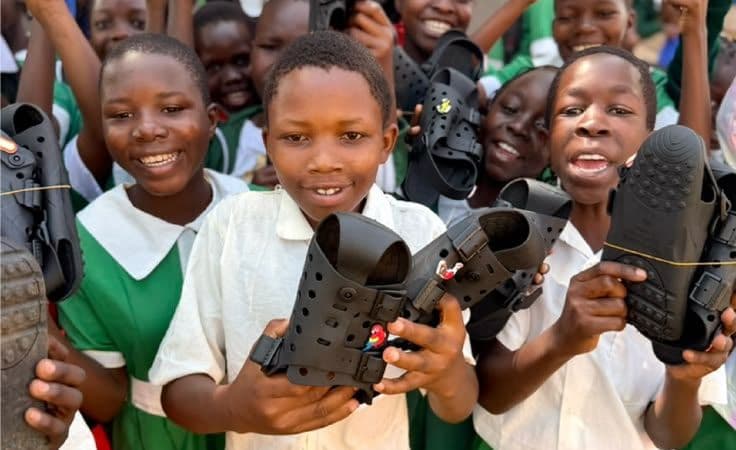 Pupils in green uniforms holding up their new shoes