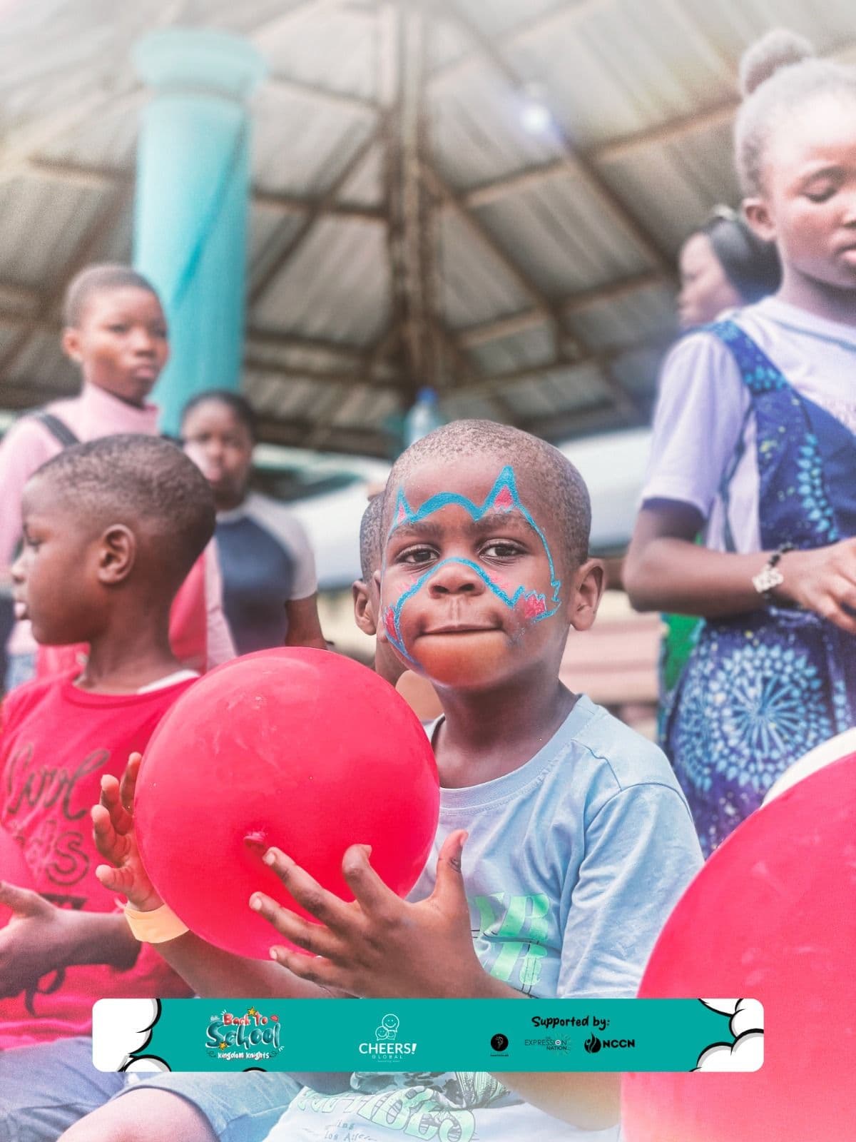 A boy with a painted face holding a red balloon at a Back to School event