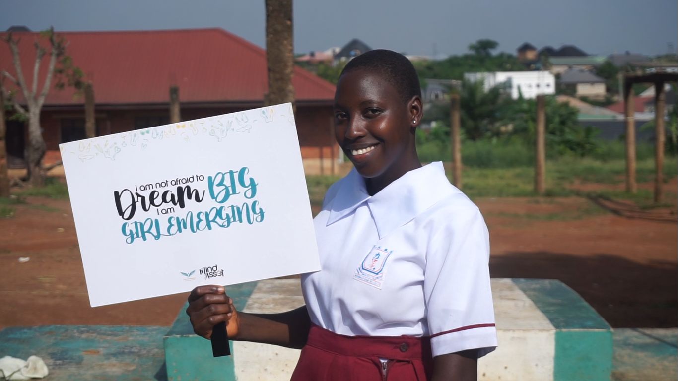 A smiling girl holding a Dream Big Girls Emerging sign